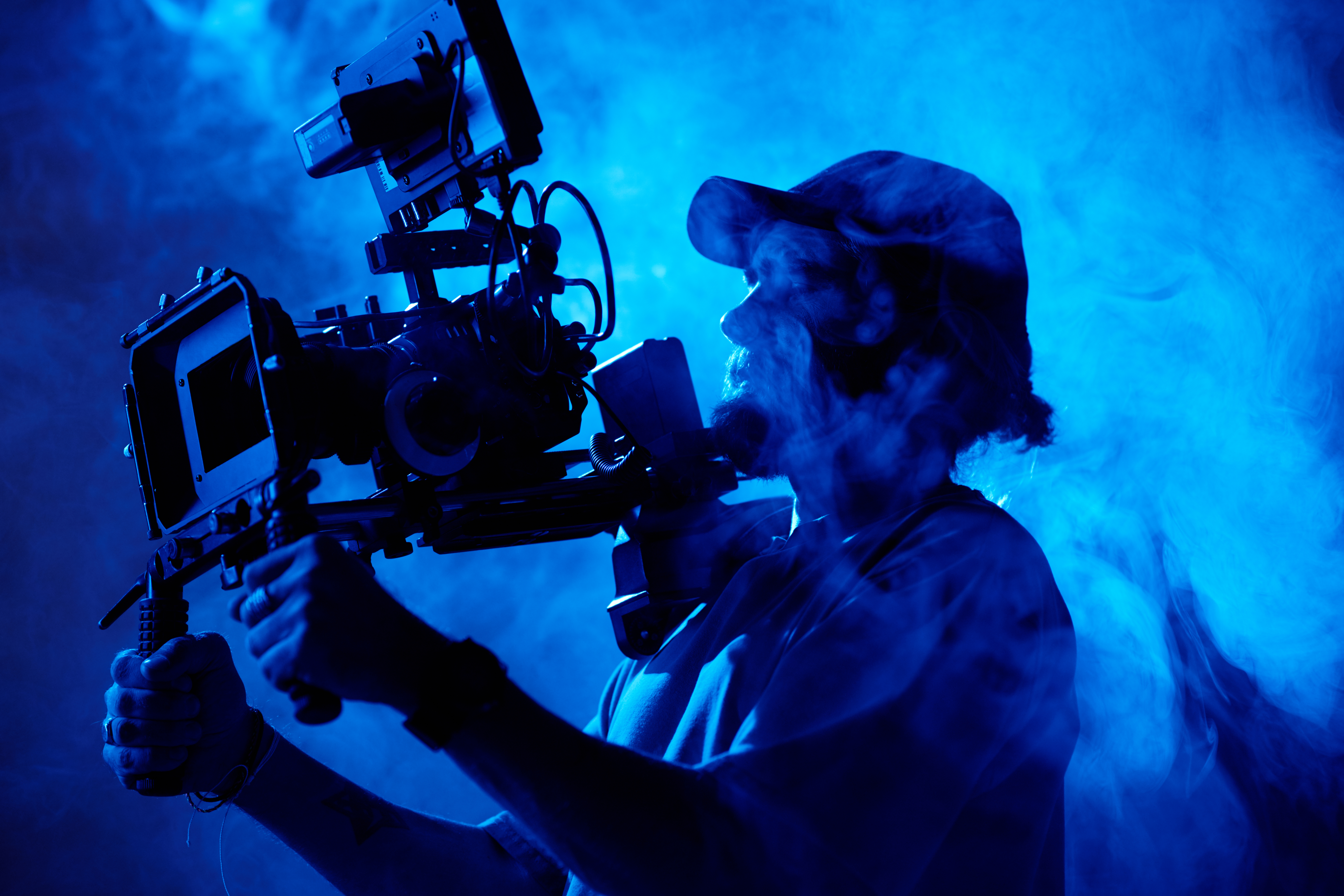 Bearded videographer in baseball cap holding steadicam while making adjustments